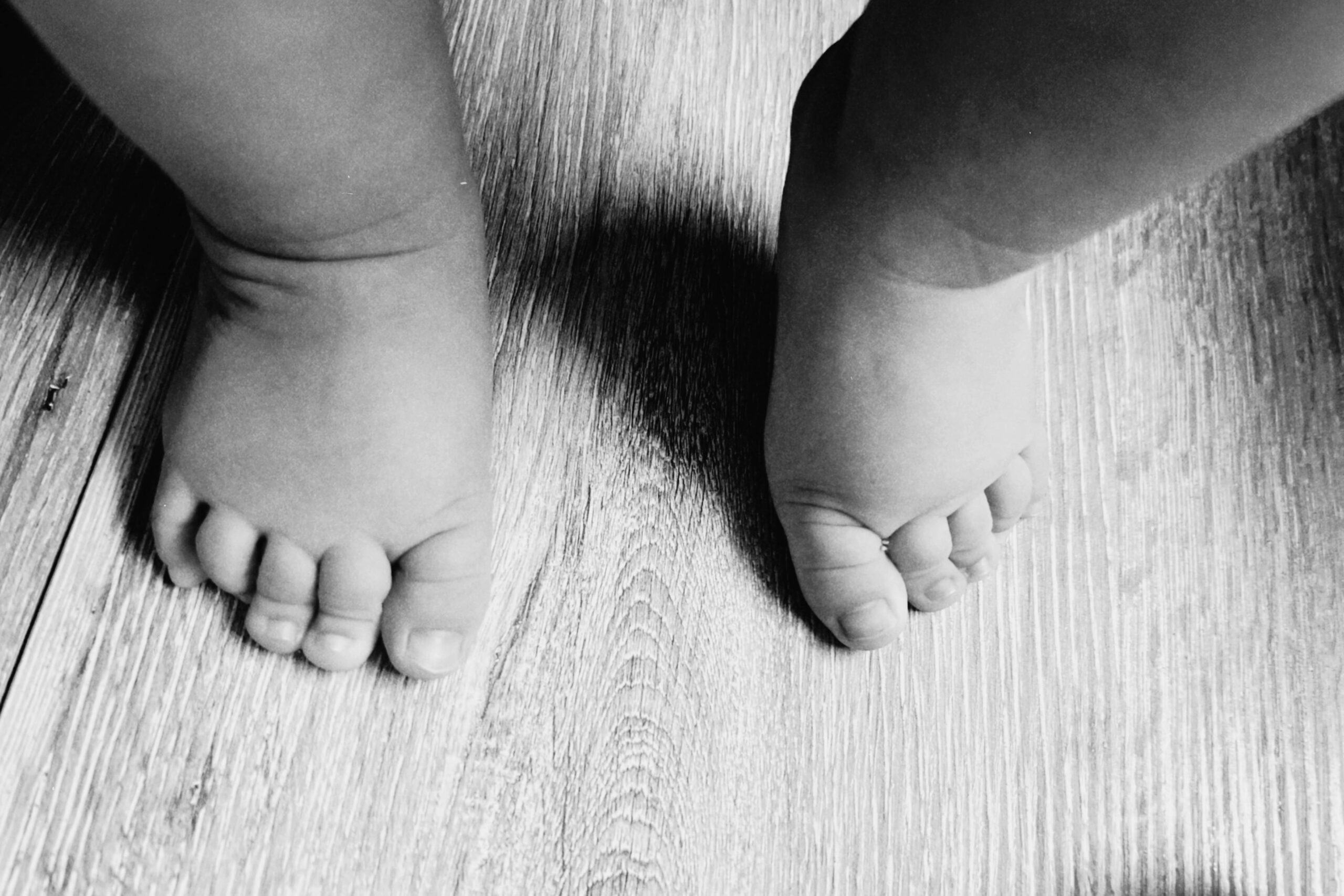 Entzückende Babyfüße, die auf einen Holzboden treten, festgehalten in Schwarzweiß.