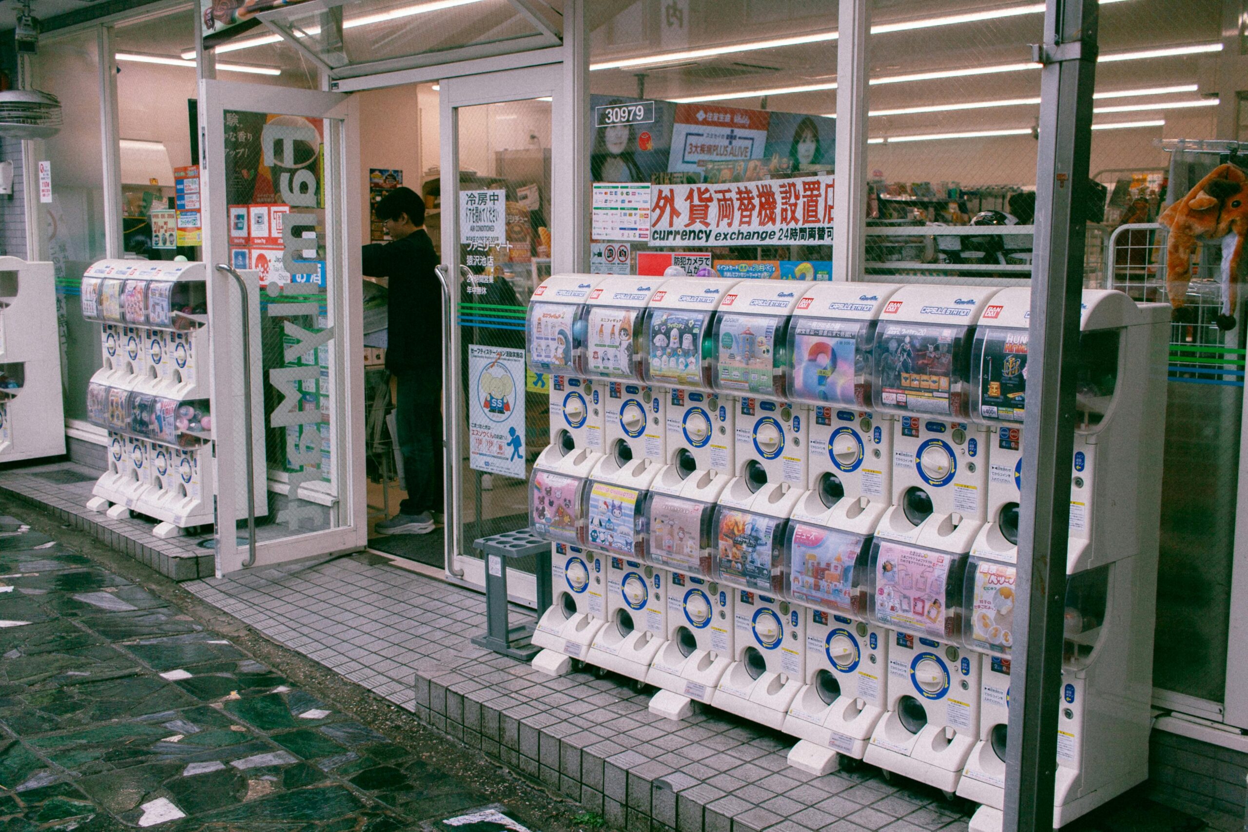 Reihen von Gashapon-Automaten vor einem japanischen Laden, die Spielzeugkapseln anbieten.